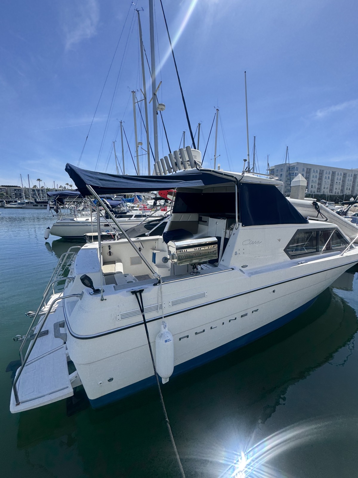The Ciera moored in Marina Del Rey on a clear morning, navy canvas top rigged over the cockpit and a stainless grill mounted on the stern rail.